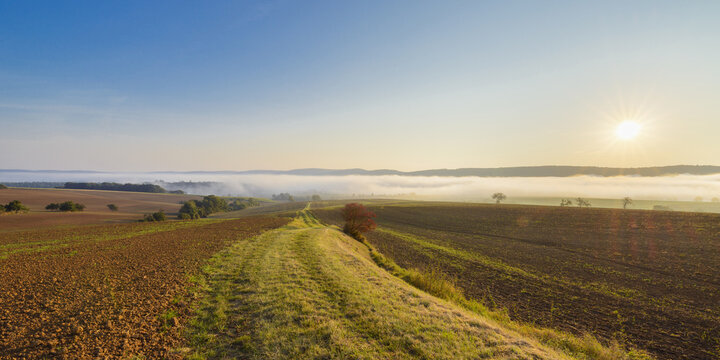 Countryside with pathway and morning mist over the fields at sunrise in the community of Grossheubach in Bavaria, Germany
