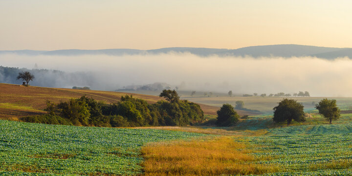 Countryside with morning mist over the fields in the community of Grossheubach with the Spessart hills in the background in Bavaria, Germany