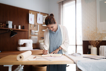 Fashion seamstress woman taking notes while using tape measure to measuring textile garment pattern