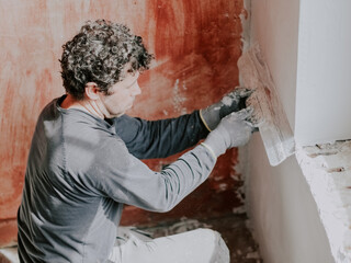 A young man is putting putty on the wall.
