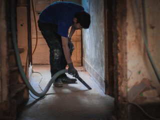 A young man vacuums a passage in a house before renovation.