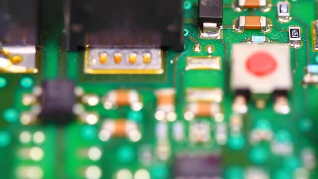 Focus in, Electronic circuit board with a red micro switch, small integrated circuit and surface mounted resistors shown as soldered on the green printed circuit card. Close up shot
