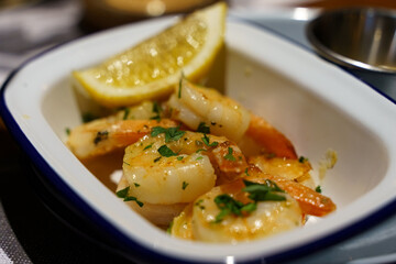 A dish of freshly prepared grilled shrimp with sauce and lemon in a white plate.