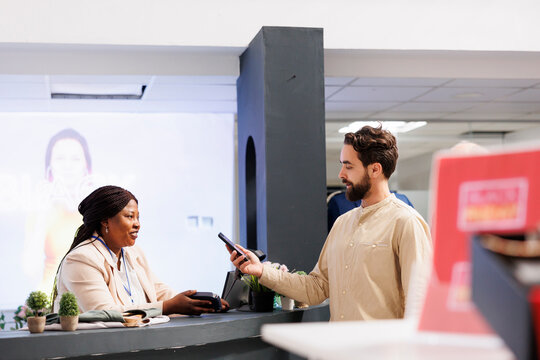 Young man standing at retail checkout counter holding smartphone paying for purchases, using nfc technology to pay for clothes while shopping in clothing store, customer making contactless payment
