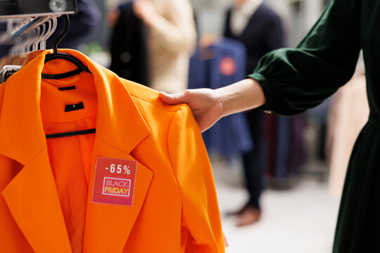 Female shopper choosing clothes in shopping center during Black Friday special offers buying clothing at discounted prices. Customer looking through rack with hanging apparel, hunting for bargains