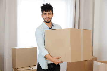 portrait of young hispanic man holding a moving box - happy young man moving
