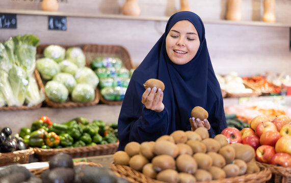 Asian girl in paranja choosing kiwi in supermarket