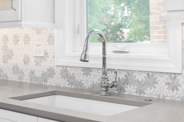 A kitchen faucet detail with a marble daisy flower tiled backsplash, white cabinets, chrome faucet,...