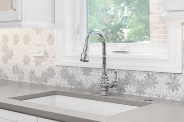 Poster A kitchen faucet detail with a marble daisy flower tiled backsplash, white cabinets, chrome faucet, and a light brown quartz countertop. © Joe Hendrickson