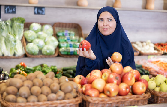 Girl in paranja making purchases in supermarket, choosing fresh ripe apples