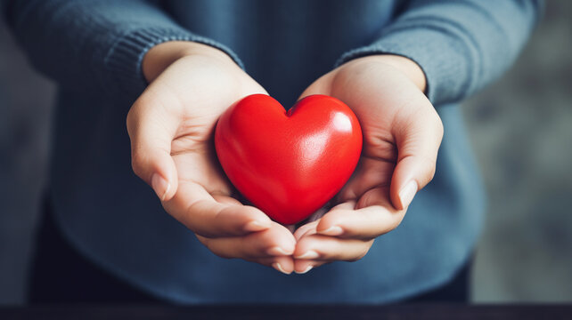 close up of woman 's hands holding red heart with blurred bokeh background. love and health care concept