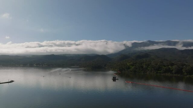 Forwards fly above water surface, beautiful nature scenery with clouds rising from forest. Athletes rowing on lake. Cachuma Lake, California, USA