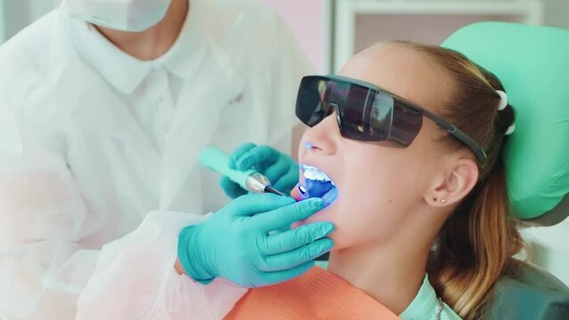 Dentist installs light-curing seal in dentistry to patient teen girl.