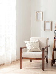 Interior Design of a Bright Mid-Century Living Room with Beige Fabric Accent Padded Armchair, Decorative Throw Pillow, and Bookshelf. White Wall with Picture Frame Mock-Ups, Wooden Flooring.