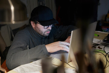 A close-up shot of a man using a laptop in a dimly lit room, engrossed in his digital work during the late hours of the night