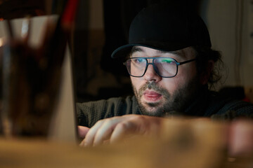 A close-up shot of a man using a laptop in a dimly lit room, engrossed in his digital work during...