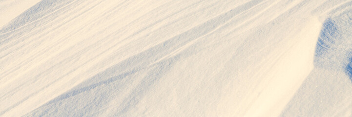 Beautiful winter background with snowy ground. Natural snow texture. Wind sculpted patterns on snow surface. Wide panoramic texture for background and design.