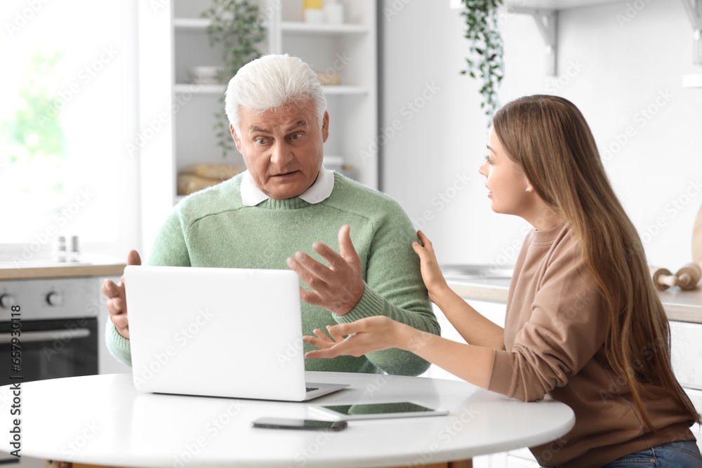 Poster senior man with his granddaughter using laptop in kitchen