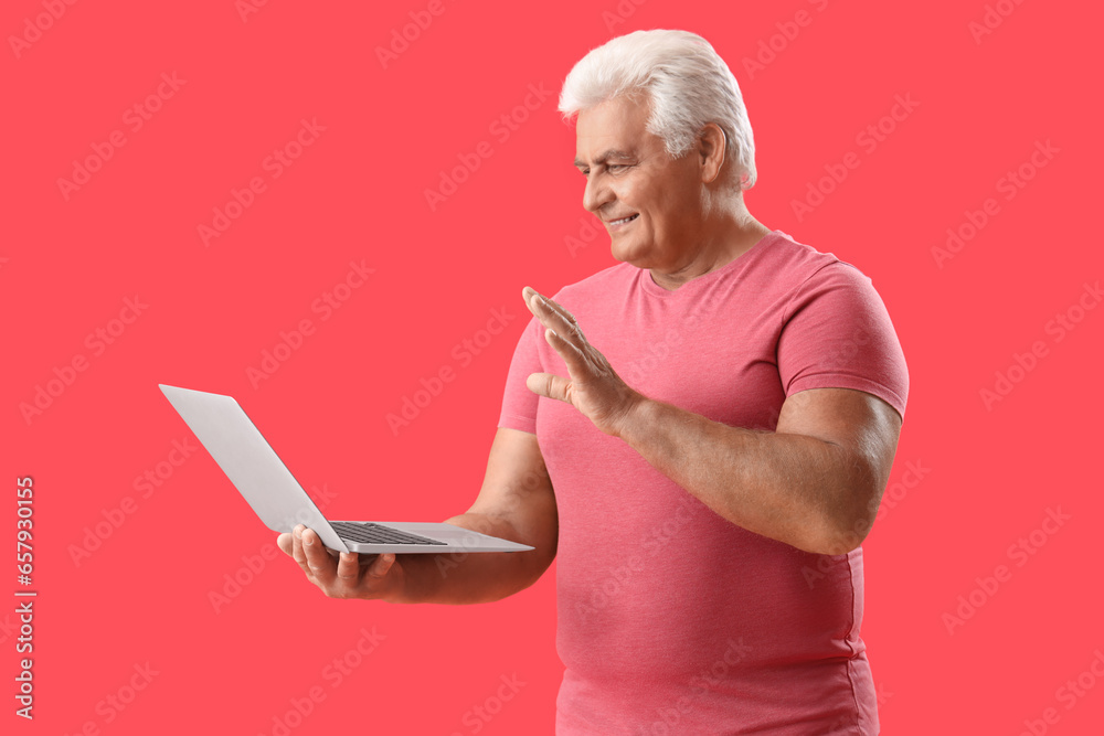 Poster Senior man with laptop video chatting on red background