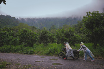 asian couples  collaborated to push a malfunctioning motorcycle in the middle of the forest road