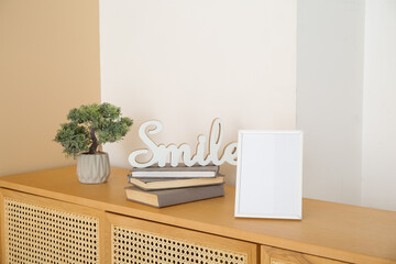 Blank frame, books and decorative tree in pot on wooden sideboard