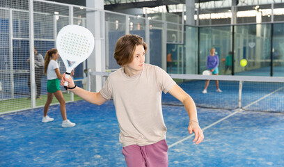 Portrait of a fifteen-year-old guy tennis player engaged in the popular sport of padel with a racket indoors