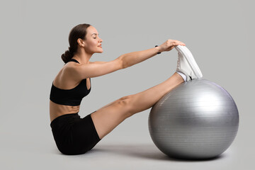 Sporty young woman training with fitball on light background