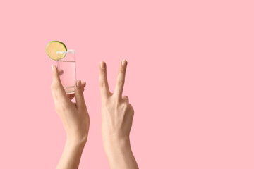 Female hands holding shot of tequila and showing victory gesture on pink background - obrazy, fototapety, plakaty