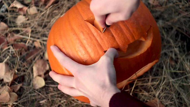 Man hand cutting pumpkin head jack lantern at all halloween. Cutting pumpkins eye with knife on the grass