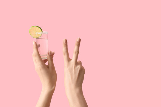 Female hands holding shot of tequila and showing victory gesture on pink background