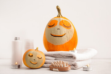 Pumpkins with clay masks and spa supplies on light background