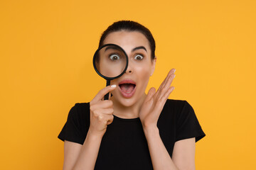 Emotional woman looking through magnifier glass on yellow background