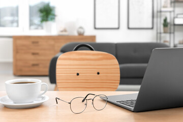 Home workspace. Laptop, glasses and cup of coffee on wooden desk in room
