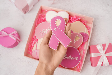 Woman holding pink cookie in shape of ribbon on white grunge background. Breast cancer awareness...