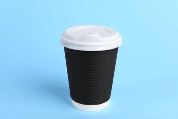 Black paper cup with plastic lid on light blue background. Coffee to go