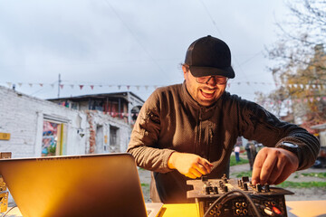 A young man is entertaining a group of friends in the backyard of his house, becoming their DJ and playing music in a casual outdoor gathering