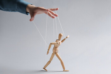Woman pulling strings of puppet on light grey background, closeup