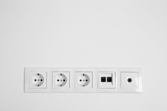 Many power sockets with ethernet and TV coax plates on white wall indoors. Space for text