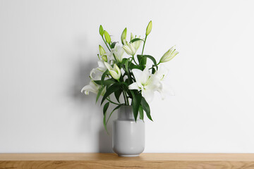 Beautiful bouquet of lily flowers in vase on wooden table near white wall