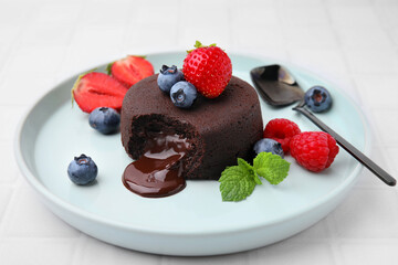 Plate with delicious chocolate fondant, berries and mint on white tiled table, closeup