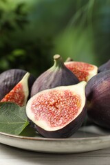 Whole and cut ripe figs with leaf on white wooden table against blurred green background, closeup