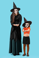 Little girl and her mother dressed for Halloween as witches with burning candles on blue background