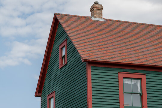 The exterior of a red wooden clapboard building with a peaked cedar shake roof. The wood wall is horizontal cape cod beveled clapboard siding. The barn has a small window with green and red trim.