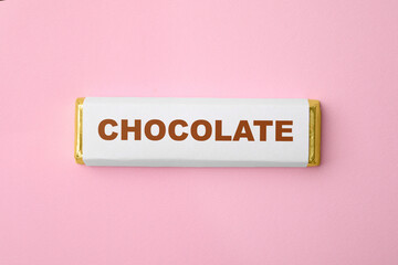 One chocolate bar in packaging on pink background, top view