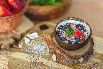 White yogurt with strawberries, blueberries, mint, grated coconut and chocolate in a coconut bowl...