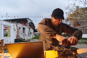 A young man is entertaining a group of friends in the backyard of his house, becoming their DJ and playing music in a casual outdoor gathering