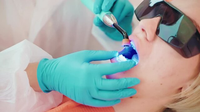 Dentist installs light-curing seal in dentistry to patient woman.