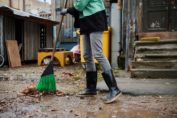 A woman diligently maintains the garden by collecting old, dry leaves, creating a picturesque scene of outdoor care and seasonal tidiness