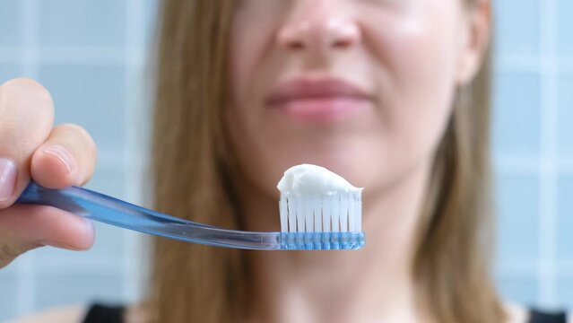 Young woman squeezing toothpaste on a toothbrush on blue background, selective focus.