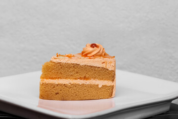 Orange cake with cream and red jelly on the top on white plate close up background